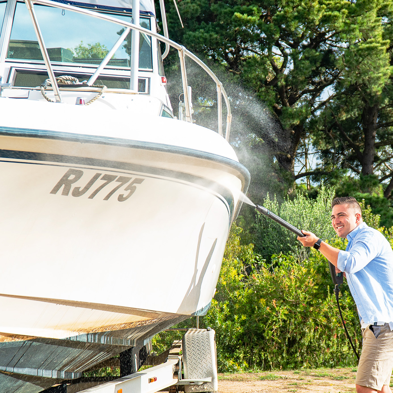 Man pressure washing a boat on a trailer outdoors