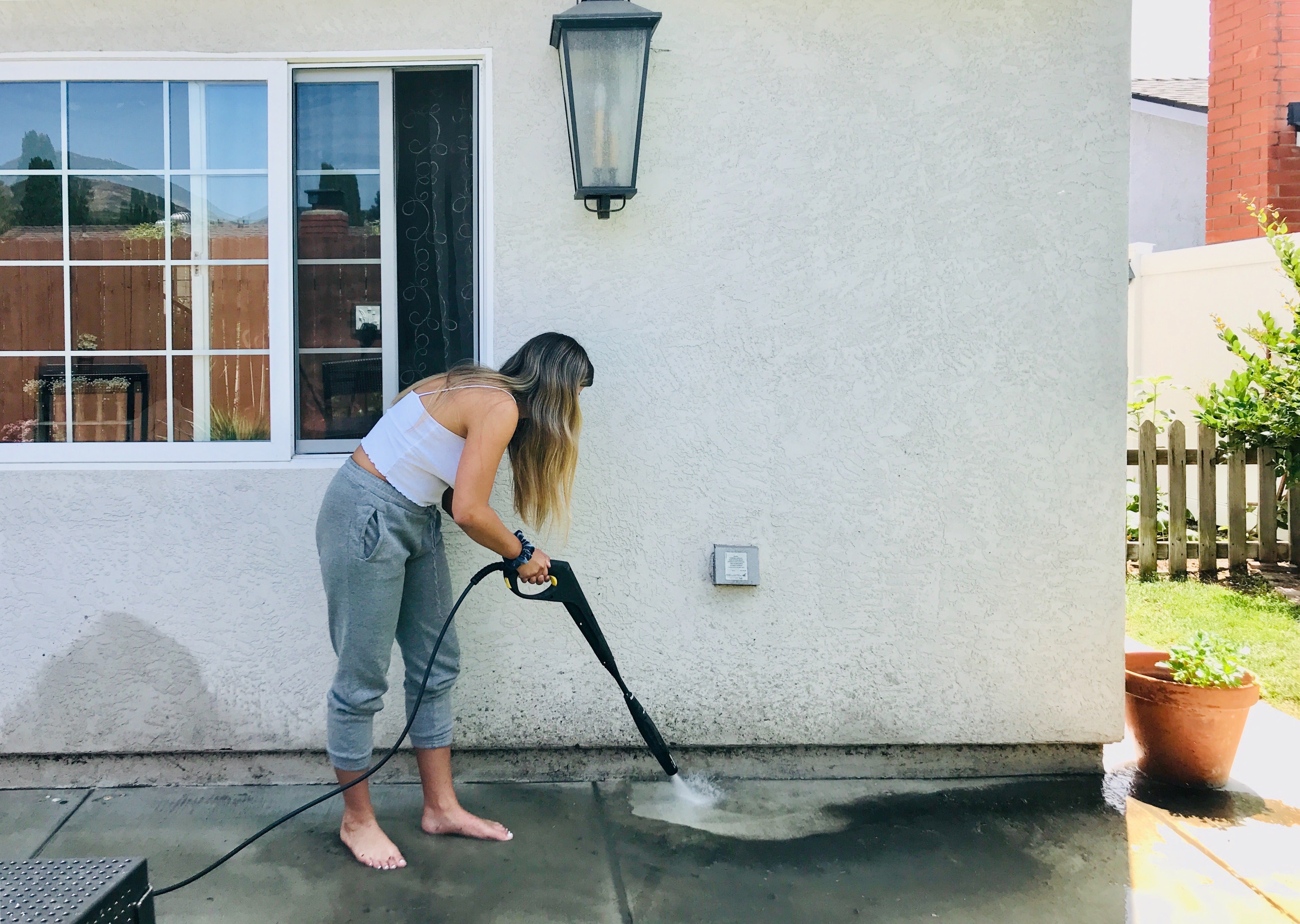 Woman pressure washing a patio outside a house