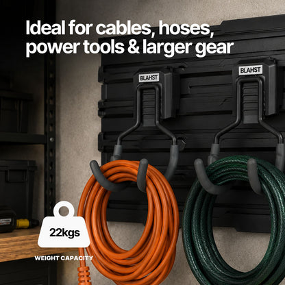 Orange and green coiled cables hanging from two BLAHST Modular Curved Hooks on a wall panel